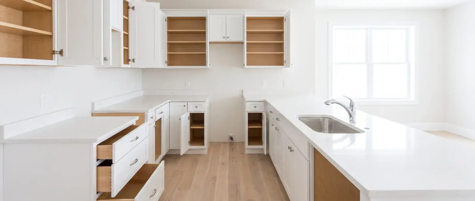 An emptied kitchen after a move-out clean, cabinet doors and drawers open on bare, wiped shelves